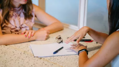 Two women chatting over table with pen and paper